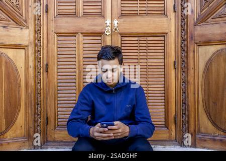 Young European man sitting in a palace and using his cell phone in Marrakesh, Morocco Stock Photo