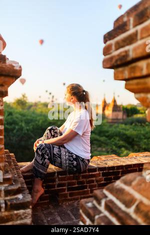Beautiful woman enjoying rooftop view of hot air balloons fly over thousands of ancient pagodas at sunrise in Bagan Myanmar Stock Photo
