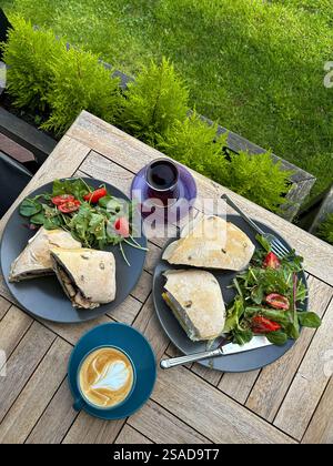 This inviting image portrays a serene outdoor breakfast setting on a wooden table. Two plates hold artisanal sandwiches with fresh greens and vibrant Stock Photo
