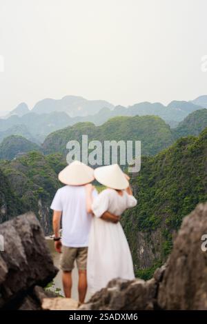 Beautiful couple enjoys travel through Southeast Asia contemplating the views of karst mountains and river of Mua Cave in Vietnam. Focus on stunning l Stock Photo