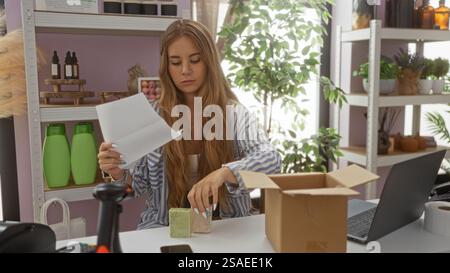 Young woman working in home decor store, examining documents and packaging items in a bright, organized indoor interior setting with decorative produc Stock Photo