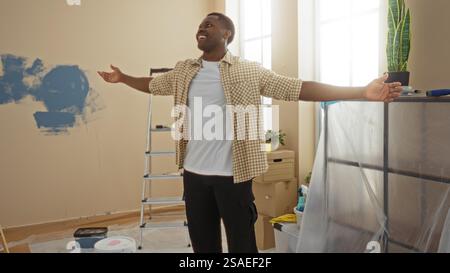Young man standing joyfully in a bright living room with arms outstretched surrounded by renovation tools evoking a sense of pride and accomplishment Stock Photo