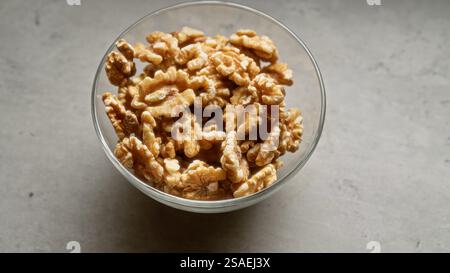 Bowl of raw walnuts on a light gray surface, showcasing healthy, nutritious, organic, shelled, and fresh nuts in a glass container, perfect for cookin Stock Photo