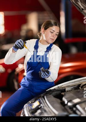 Female auto mechanic checking oil level in car engine Stock Photo