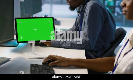 Close up of green tablet in server room used by system administrators to ensure minimal downtime. Data center software developers looking at chroma key device, monitoring performance, camera A Stock Photo