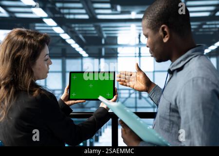 Computer scientists in data center use green screen tablet to calibrate energy usage. Team of server room IT experts using mockup device to inspect UPS configurations, doing maintenance on gear Stock Photo