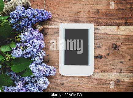 E-book on wooden background with lilac branches. Flat lay, top view. Template for feminine blog social media. Stock Photo