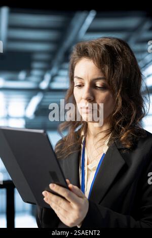 Technician in data center workspace using tablet, configuring network virtualization. Woman in server room updating storage arrays with device, verifying settings to maintain stable performance Stock Photo