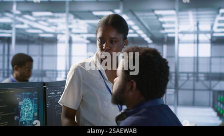 Manager taking feedback from data center engineer maintaining company network infrastructure. Team leader in server hub listening worker ensuring optimal system performance, camera A Stock Photo