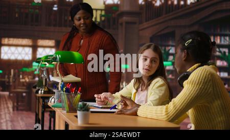 Teacher assisting scholars with class homework for mentoring session, providing academic instruction and support to help with the curriculum. Tutor lecturer gives private lessons. Camera B. Stock Photo