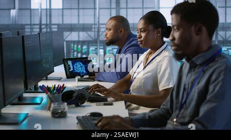 Technicians using computers and tablet in data center, implementing AI systems. Server farm experts using artificial intelligence on device to identify hardware failures impacting operations, camera A Stock Photo