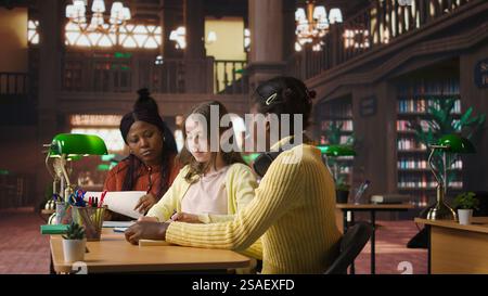 Preteens girls and their professor collaborating on schoolwork at the library, focused on academic materials to write a good essay. Students collect extra information with private lessons. Camera A. Stock Photo