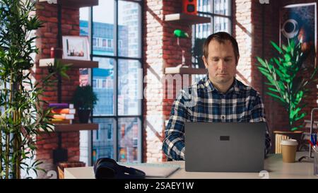 Employee completing spreadsheets on laptop and listening music. Worker in home office wearing headphones editing documents on notebook, updating reports and files, camera A Stock Photo