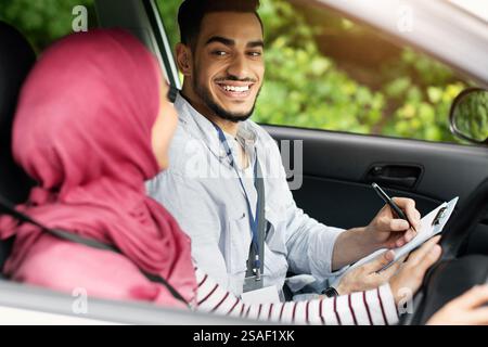 Driving School Test. Handsome Young Arab Instructor Examining Muslim Female Drive Stock Photo