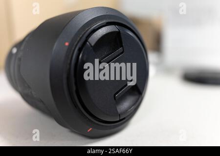 A detailed view of a camera lens highlighting its surface texture and design elements. This lens is resting on a flat surface with blurred objects in Stock Photo