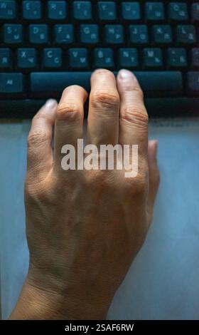 A focused hand is resting above a dark keyboard, likely working on a computer task. The environment appears calm, suggesting concentration on the work Stock Photo