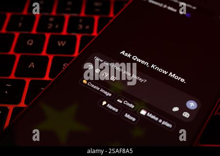 Alibaba's Qwen AI interface seen on the screen of smartphone placed on keyboard lit in red and reflection of the flag of China. Concept. Stafford, UK, Stock Photo