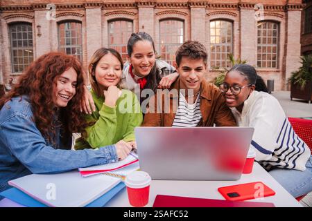 Enthusiastic Students Collaborating on a Laptop While Studying Together and Sharing Ideas in a Bright and Engaging Learning Environment Surrounded by Friends and Classmates at Their University Campus. High quality photo Stock Photo