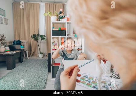 boy smiling and look at camera with speech therapy exercises in a bright educational office with a female therapist, concept of childhood development Stock Photo