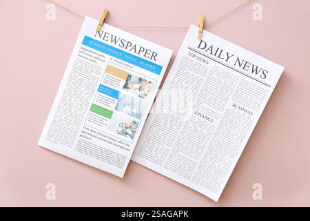 Different newspapers hanging on rope against pink background Stock Photo