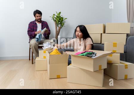 Creating lasting memories in their new nest. Happy young family couple renters tenants engaged in packing up things to boxes containers before orderin Stock Photo
