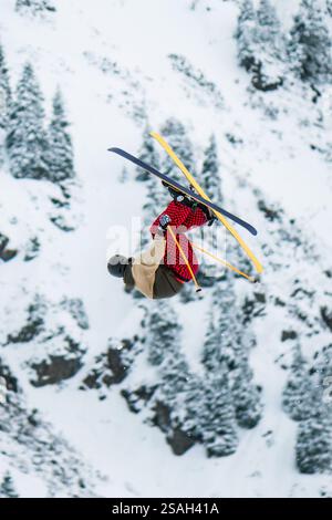 A skier performs a complicated trick in jumping big air in snow park at ski resort. A skier in a helmet, light jacket and red trousers does a somersau Stock Photo