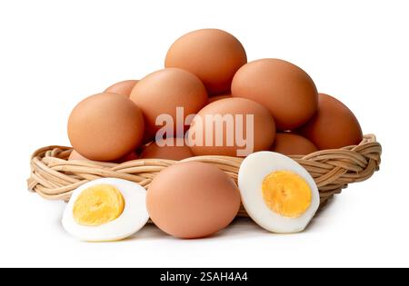 Large group of raw brown chicken eggs and peeled cooked or boiled eggs with egg yolk in two halves in stack in wicker basket is isolated on white Stock Photo