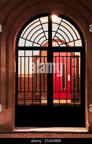 Building door with metalized abstract grill and red elevator in the background in Spain Stock Photo