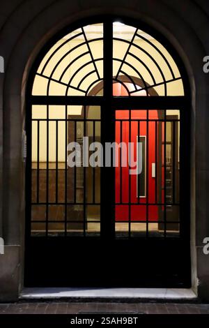 Building door with metalized abstract grill and red elevator in the background in Spain Stock Photo