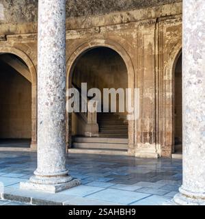 A serene architectural interior featuring stone columns and arched doorways leading to a staircase. The warm tones of the stone create a historic ambi Stock Photo