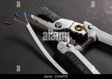 Removing the insulation from the conductor using a tool. Wire stripping tool on dark background. Stock Photo