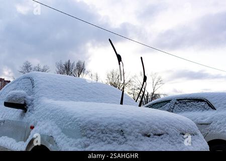 A car under snow with wipers raised up. Cars in snowdrifts after snowfall. Extreme weather conditions in wintertime. Automobiles in frosty blizzard. Stock Photo