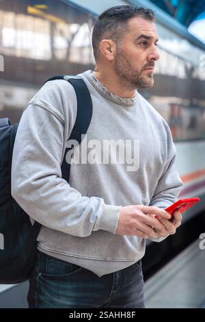Focused Man with Backpack Using Smartphone at Train Station.Vertical Stock Photo