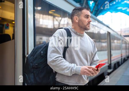 Focused Man with Backpack Using Smartphone at Train Station Stock Photo