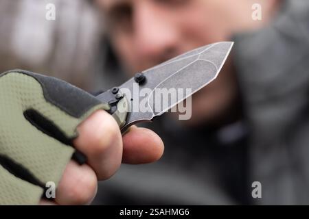 The man wearing tactical gloves using folding knife. Stock Photo
