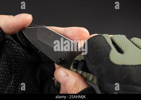 The man wearing tactical gloves using folding knife. Stock Photo