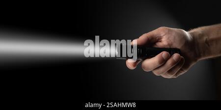 Black flashlight in human hands on a black background, including a white beam. Stock Photo