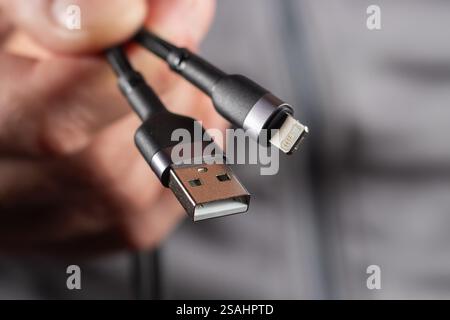 charging cables for phone in hand on gray background. Stock Photo