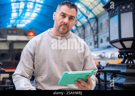 Focused Man Using Tablet While Waiting at Train Station Stock Photo