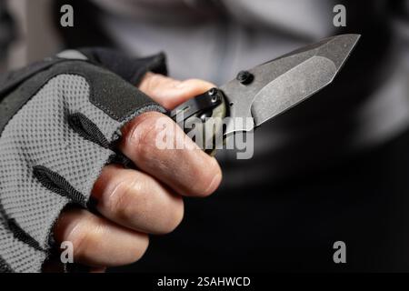 The man wearing tactical gloves using folding knife. Stock Photo