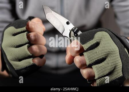 The man wearing tactical gloves using folding knife. Stock Photo