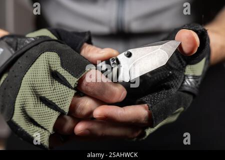 The man wearing tactical gloves using folding knife. Stock Photo