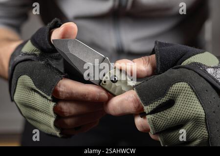 The man wearing tactical gloves using folding knife. Stock Photo