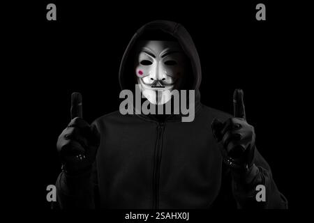 Man with anonymous mask with sweatshirt in gloves, looking at camera and show fingers up. Stock Photo