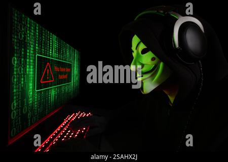 Dnipro. Ukraine. 03 feb 2024: Anonymous computer hacker in white mask and hoodie. Obscured dark face using computer for cyber attack, Data thief, inte Stock Photo