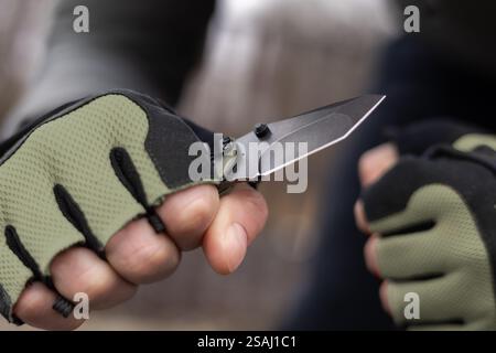 The man wearing tactical gloves using folding knife. Stock Photo