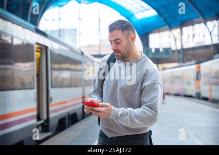 Man Using Smartphone While Waiting at Train Station Stock Photo