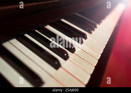 Shallow focus against closeup view of vintage piano keyboard in red light suggestive ambiance Stock Photo