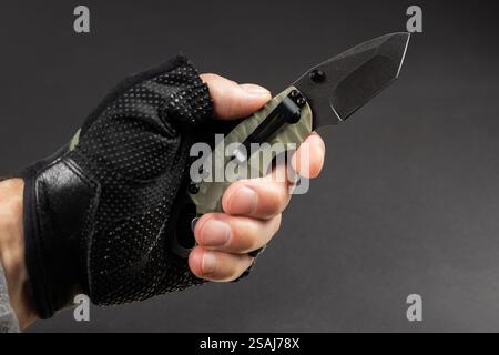 The man wearing tactical gloves using folding knife. Stock Photo