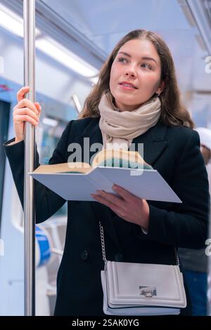 Young Woman Reading a Book While Standing on a Subway Train.Vertical Stock Photo